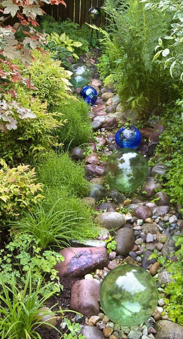 The rock-lined swale is both design feature and effective rain garden. It soaks up runoff in this wet, steep-slope garden. Glass floats further the look of a dry streambed.
